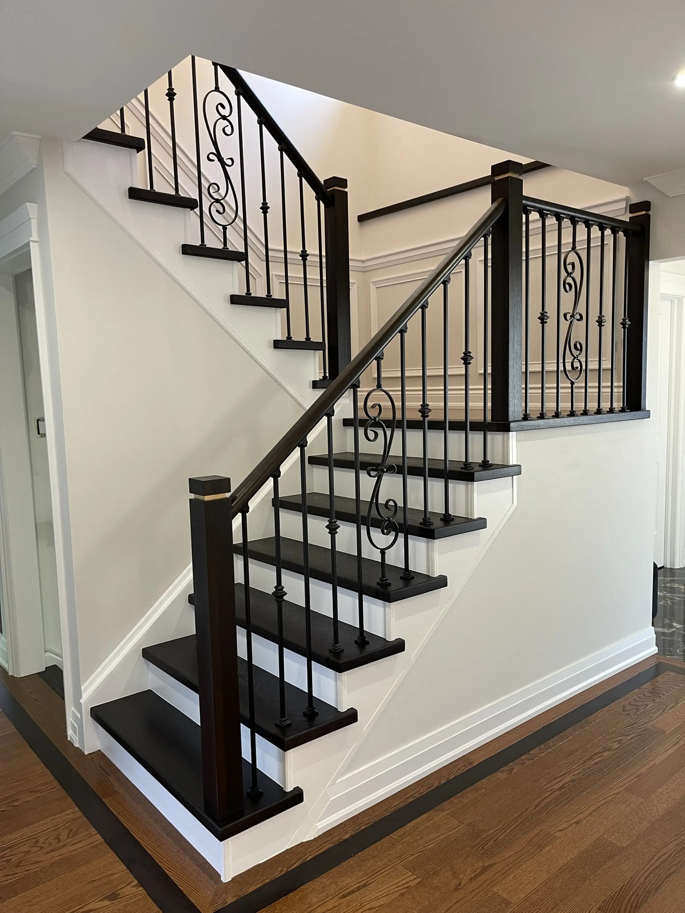 A grand staircase with dark wood steps, intricate wrought iron balusters, and bright white walls for contrast.