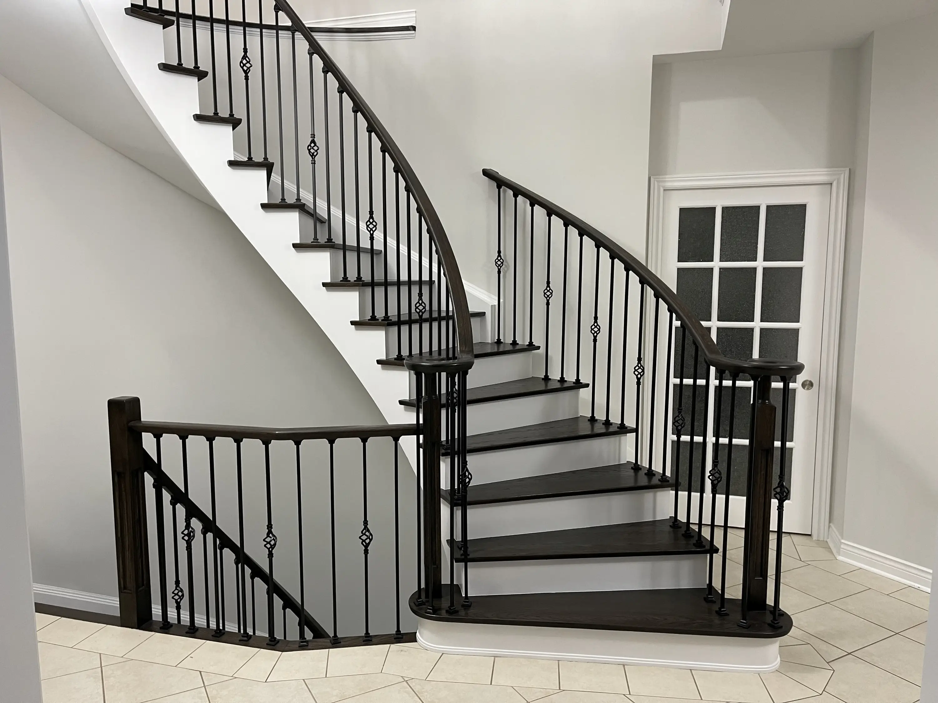 A curved staircase with dark wood treads, white risers, and decorative black balusters, framed by clean white walls.