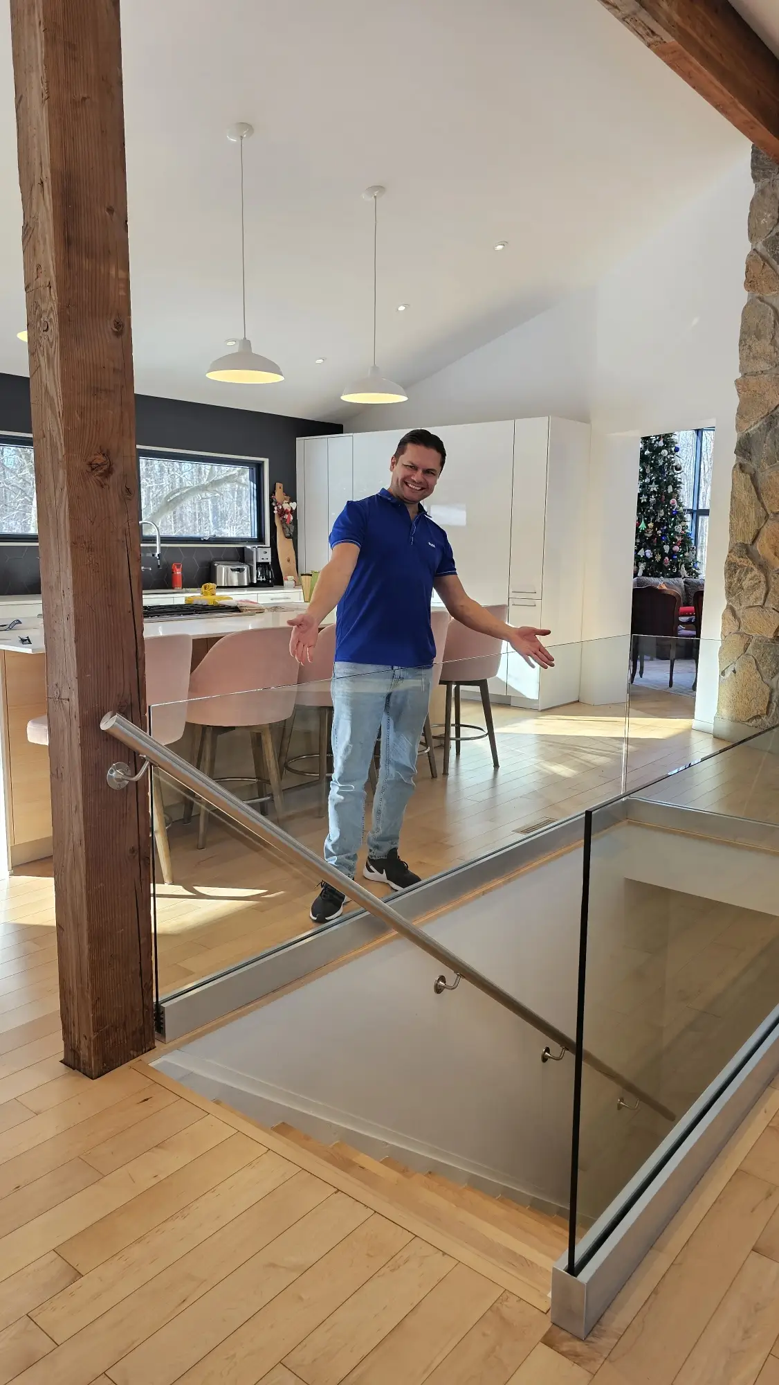 A staircase with glass railings and a stainless steel handrail, opening into a bright space with wood floors and a stone accent wall.
