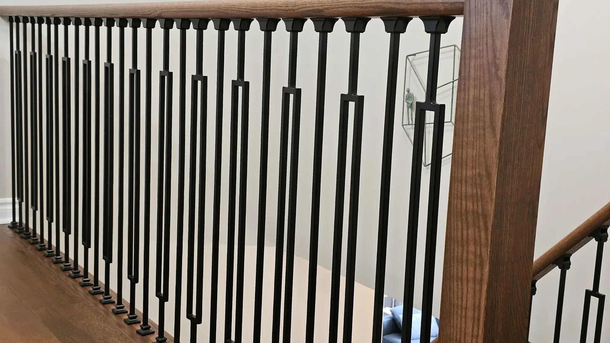 Stair railing installation with wood handrail and black balusters.