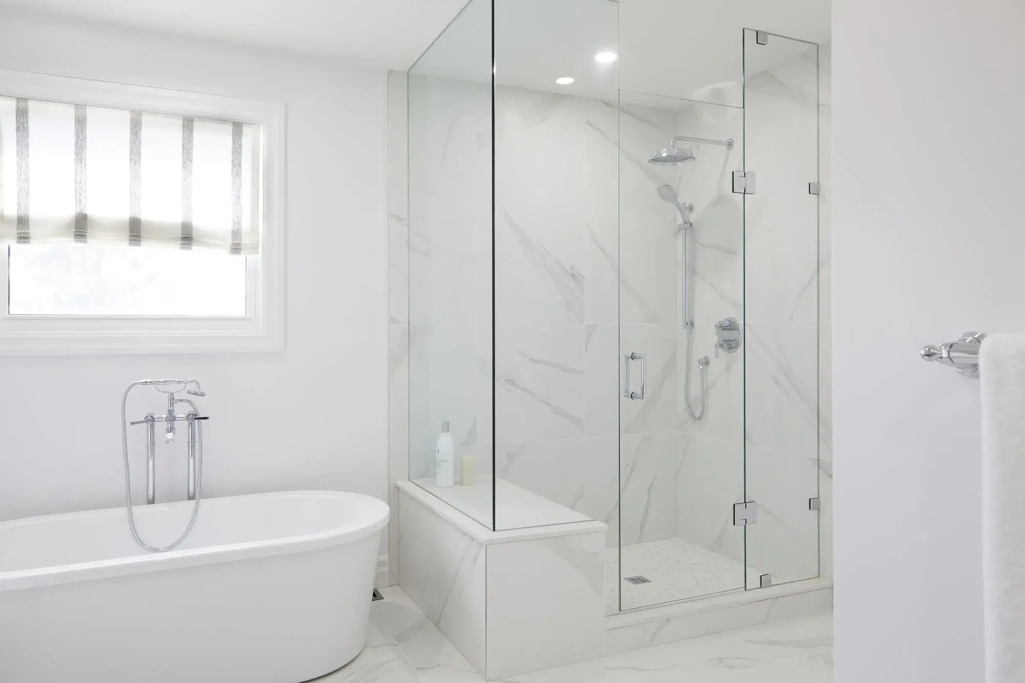 Bathroom renovation with freestanding tub, frameless glass shower, marble-look tile, chrome fixtures, and bright natural light.