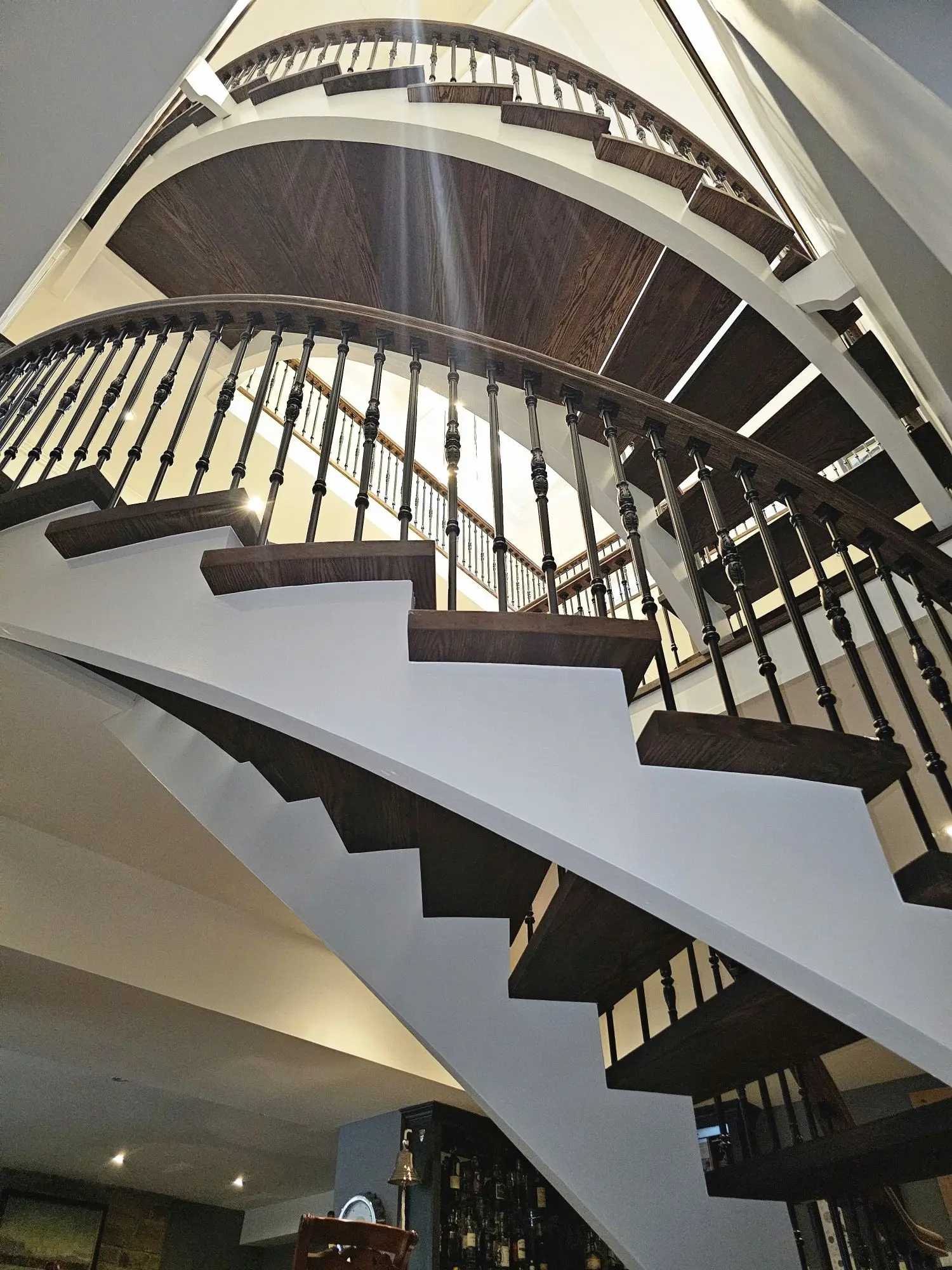 Curved staircase refinishing in Toronto with dark treads and iron railing.