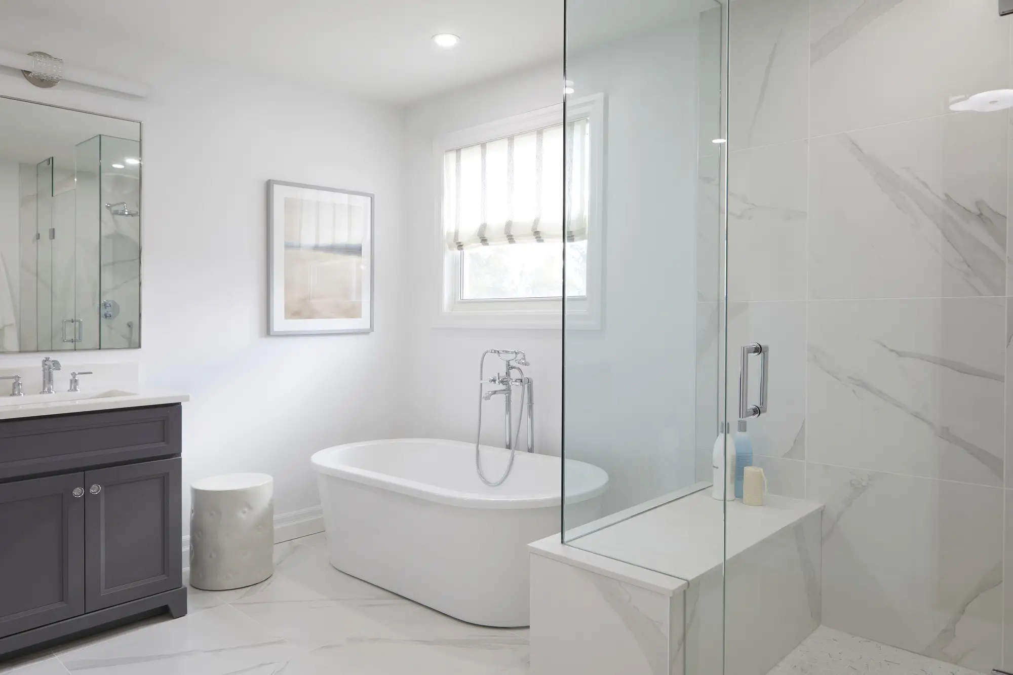 A luxurious renovated bathroom with a freestanding soaking tub, glass-enclosed shower with marble walls, and a built-in bench.
