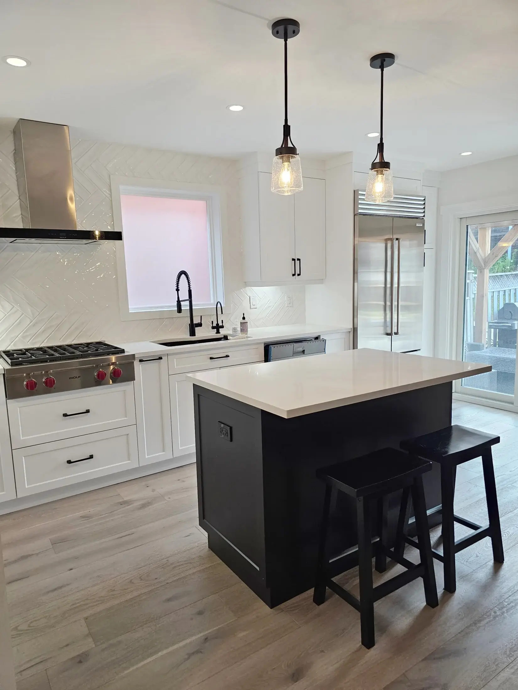 Black island and white kitchen with built-in refrigerator, pendant lights, quartz counters, and custom cabinetry in Woodbridge.