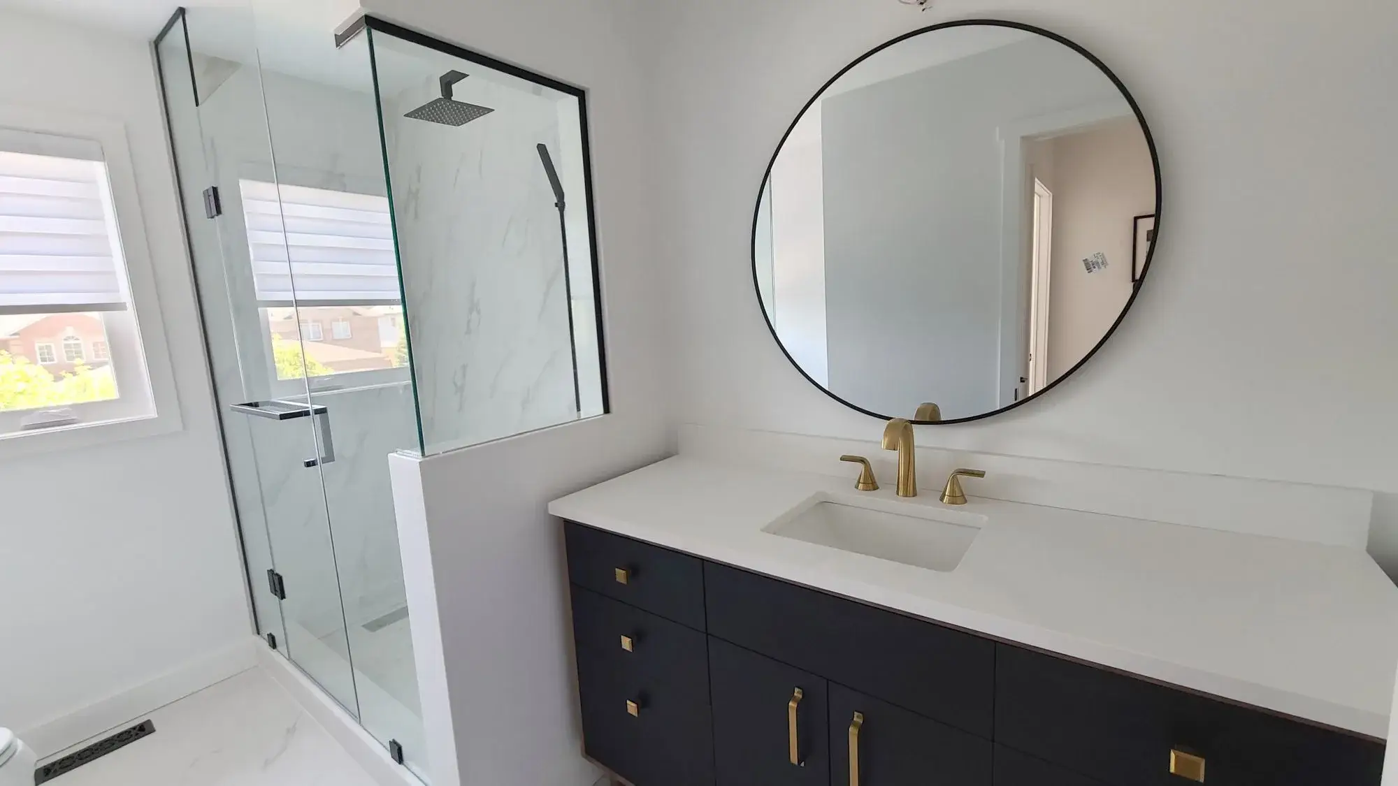 Black vanity bathroom renovation with round mirror, brass faucet, frameless glass shower, and white tile in Woodbridge.