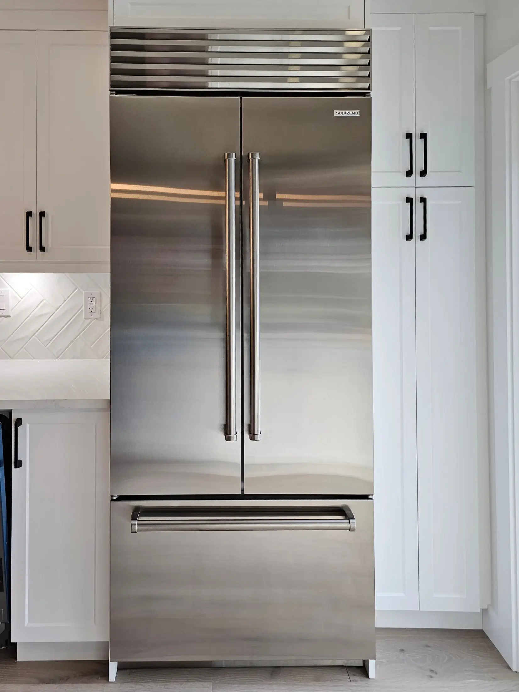 Built-in stainless refrigerator with surrounding pantry cabinets in a white kitchen with black hardware in Vaughan.