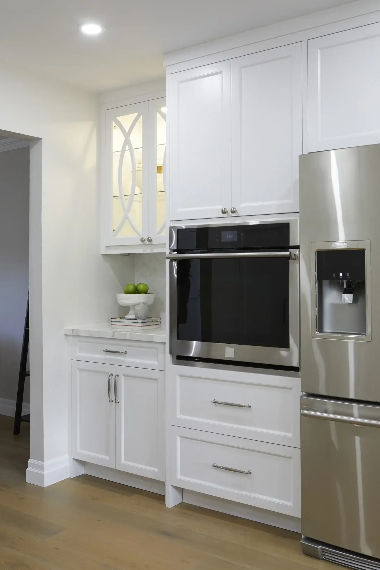 Built-in wall oven with glass display cabinets, stainless refrigerator, white shaker cabinetry, and quartz counter detail in Vaughan.