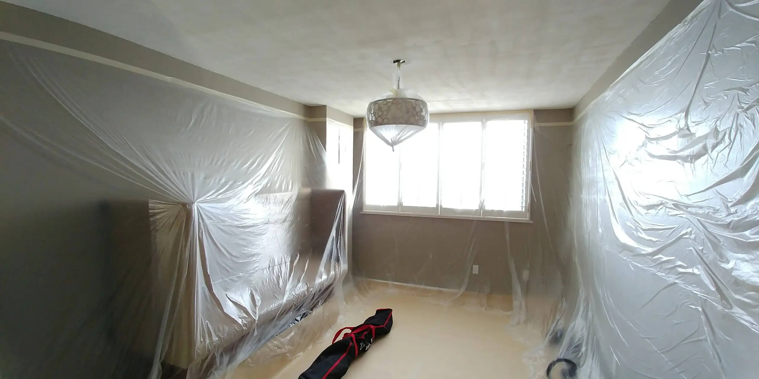 A protected room prepared for ceiling refinishing, with furniture and fixtures carefully covered to ensure a dust-free renovation process.