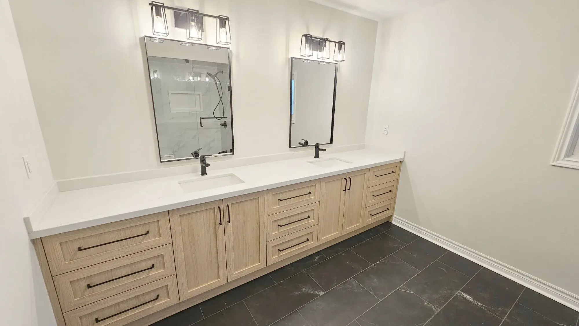 Double vanity bathroom renovation with oak cabinets, two mirrors, quartz counter, wall sconces, and dark tile floor in Vaughan.