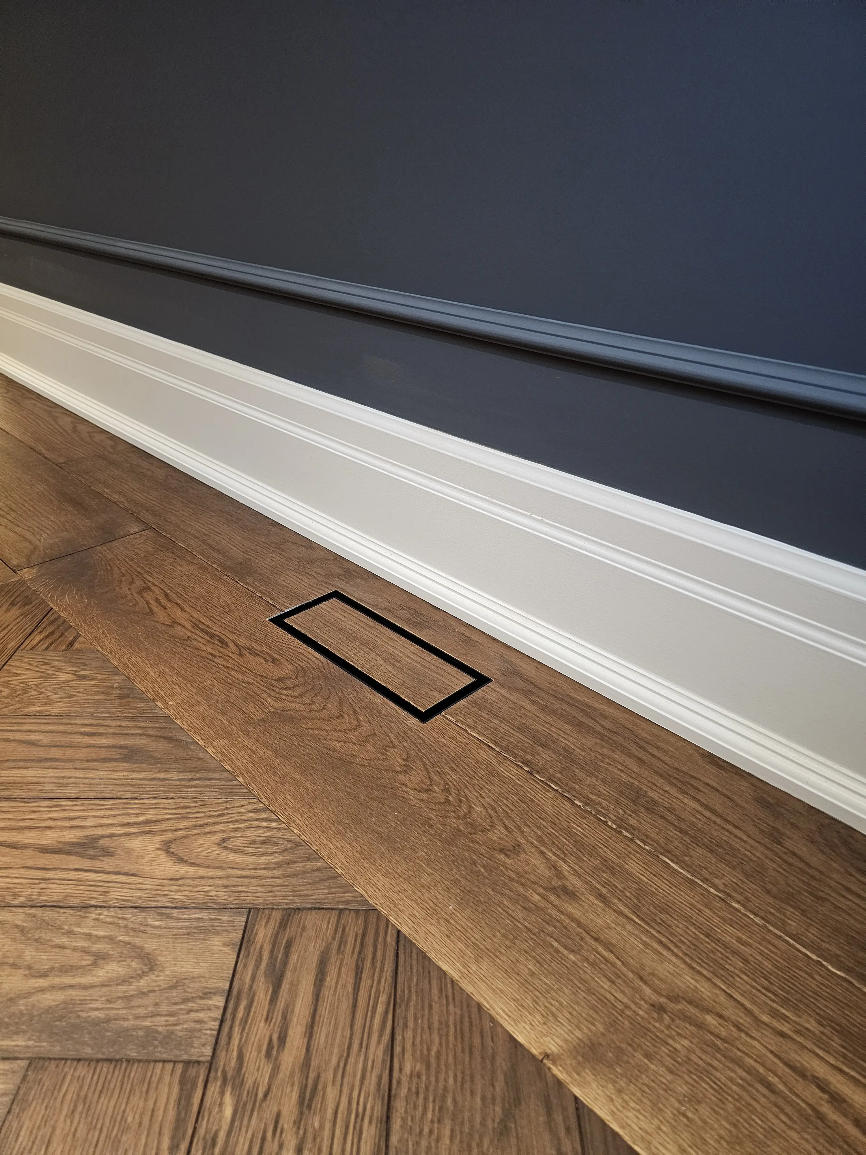 Flush wood floor vent set into herringbone hardwood flooring.