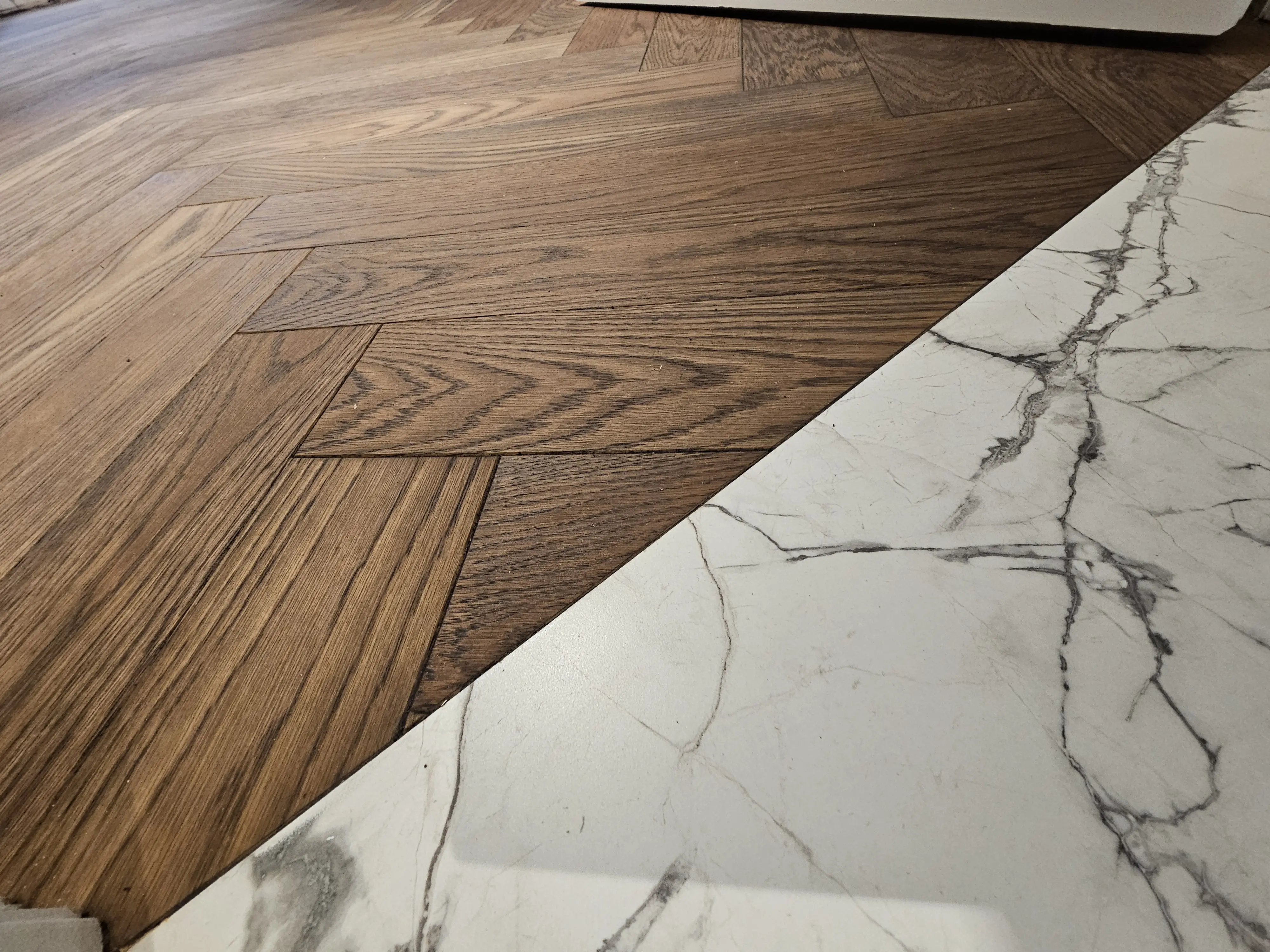 Herringbone hardwood flooring with a precise border meeting marble-look tile.