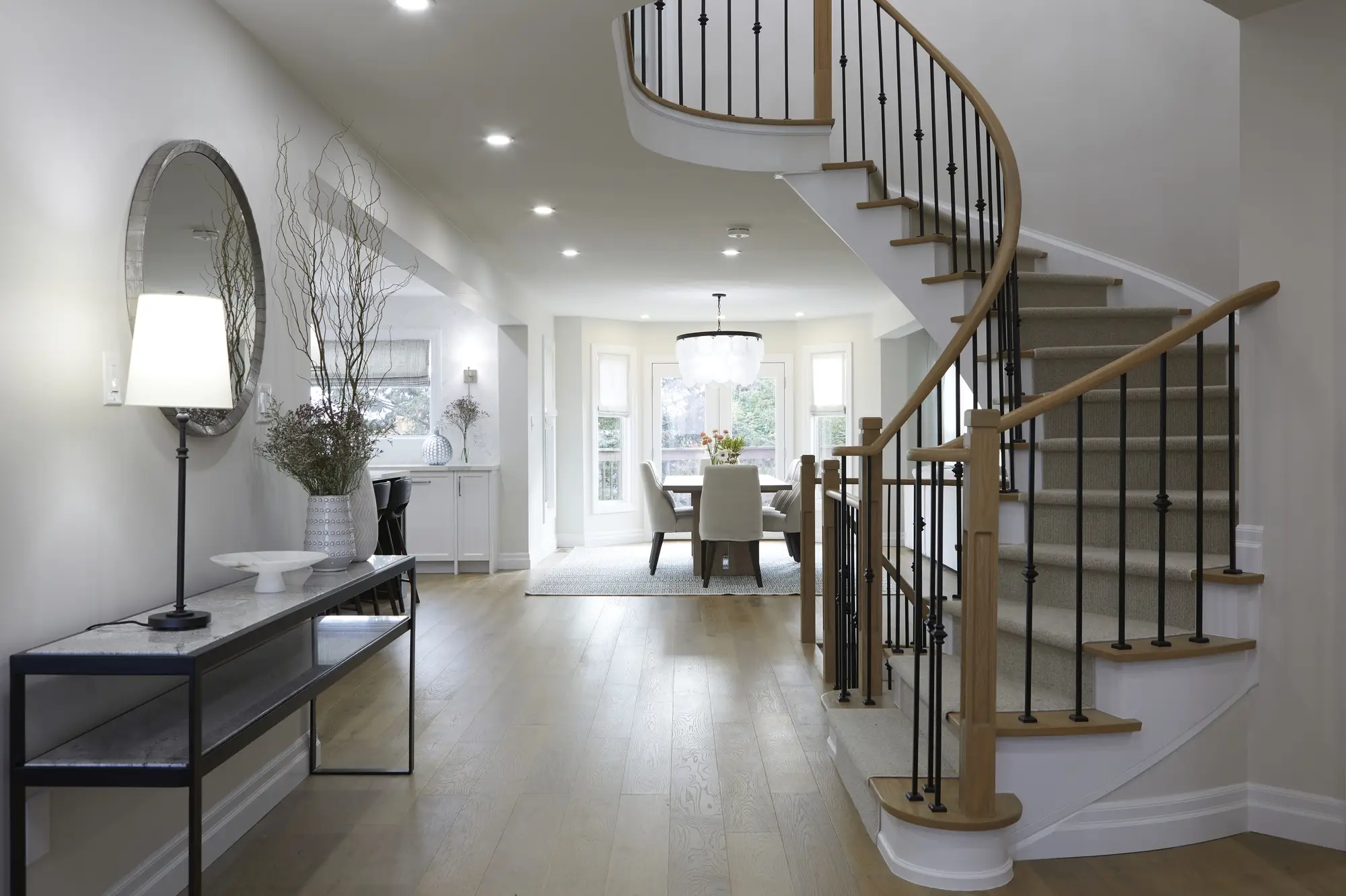 Light oak engineered hardwood flooring coordinated with a curved staircase and black iron railings.