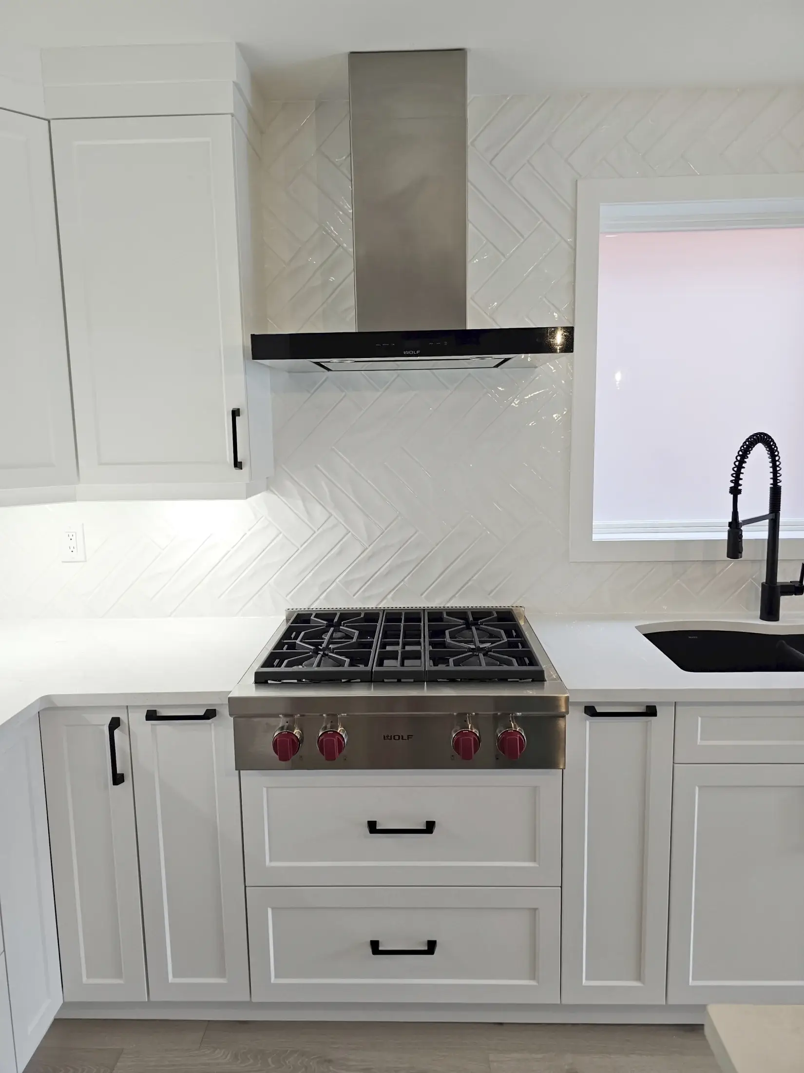 Range hood and herringbone backsplash detail in a white shaker kitchen with black hardware in Toronto.