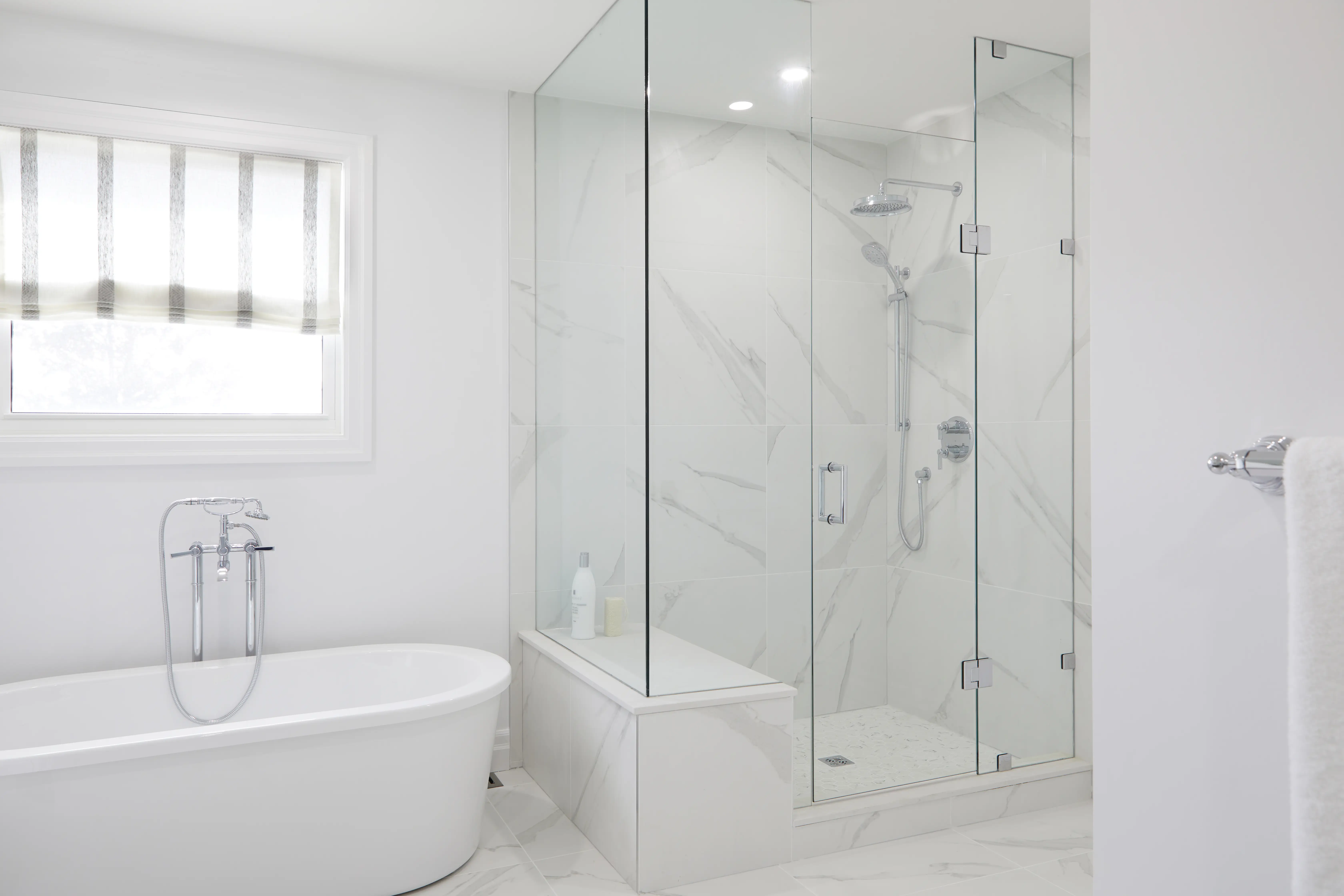 A luxurious renovated bathroom with a freestanding soaking tub, glass-enclosed shower with marble walls, and a built-in bench.