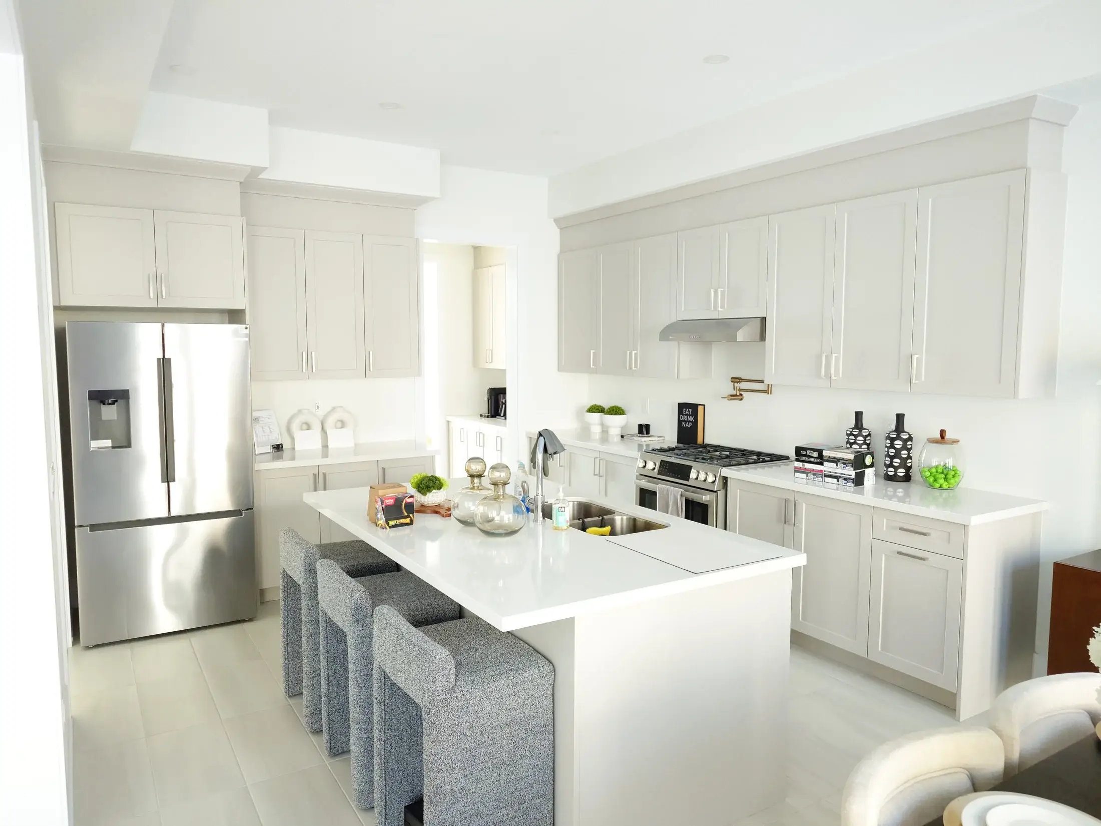 White custom kitchen with large quartz island, stainless refrigerator, grey island seating, tall pantry cabinets, and bright open layout in Vaughan.