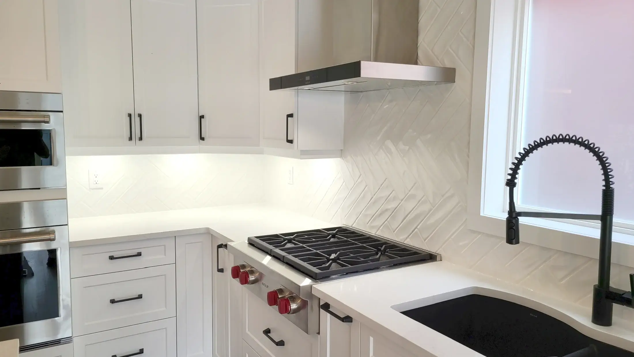 White shaker kitchen with herringbone backsplash, black faucet, range hood, and quartz counters in Woodbridge.
