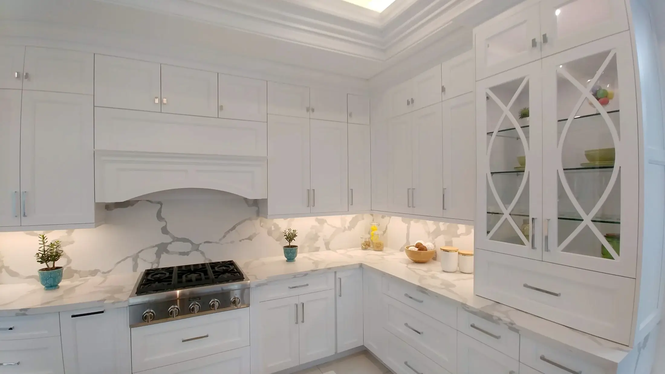 White shaker kitchen with quartz slab backsplash, glass display cabinets, and integrated storage in Toronto.