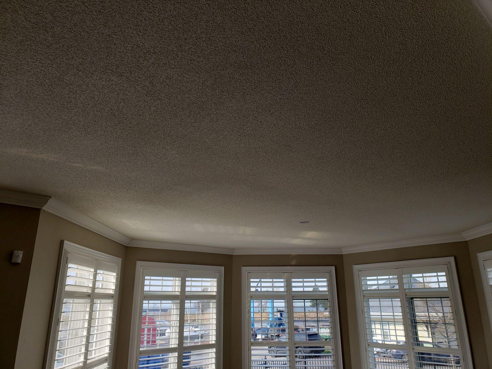 Popcorn-textured ceiling at a bay window before removal and smooth-ceiling finishing.