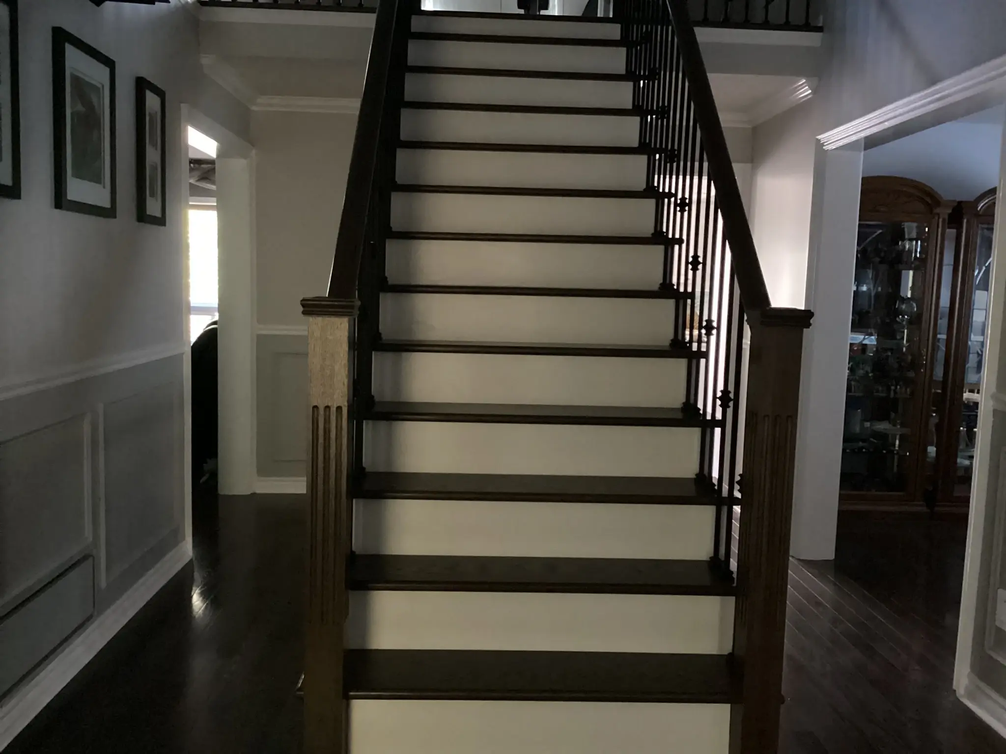Staircase after renovation with dark wood treads, white risers, black iron balusters and stained newel posts.
