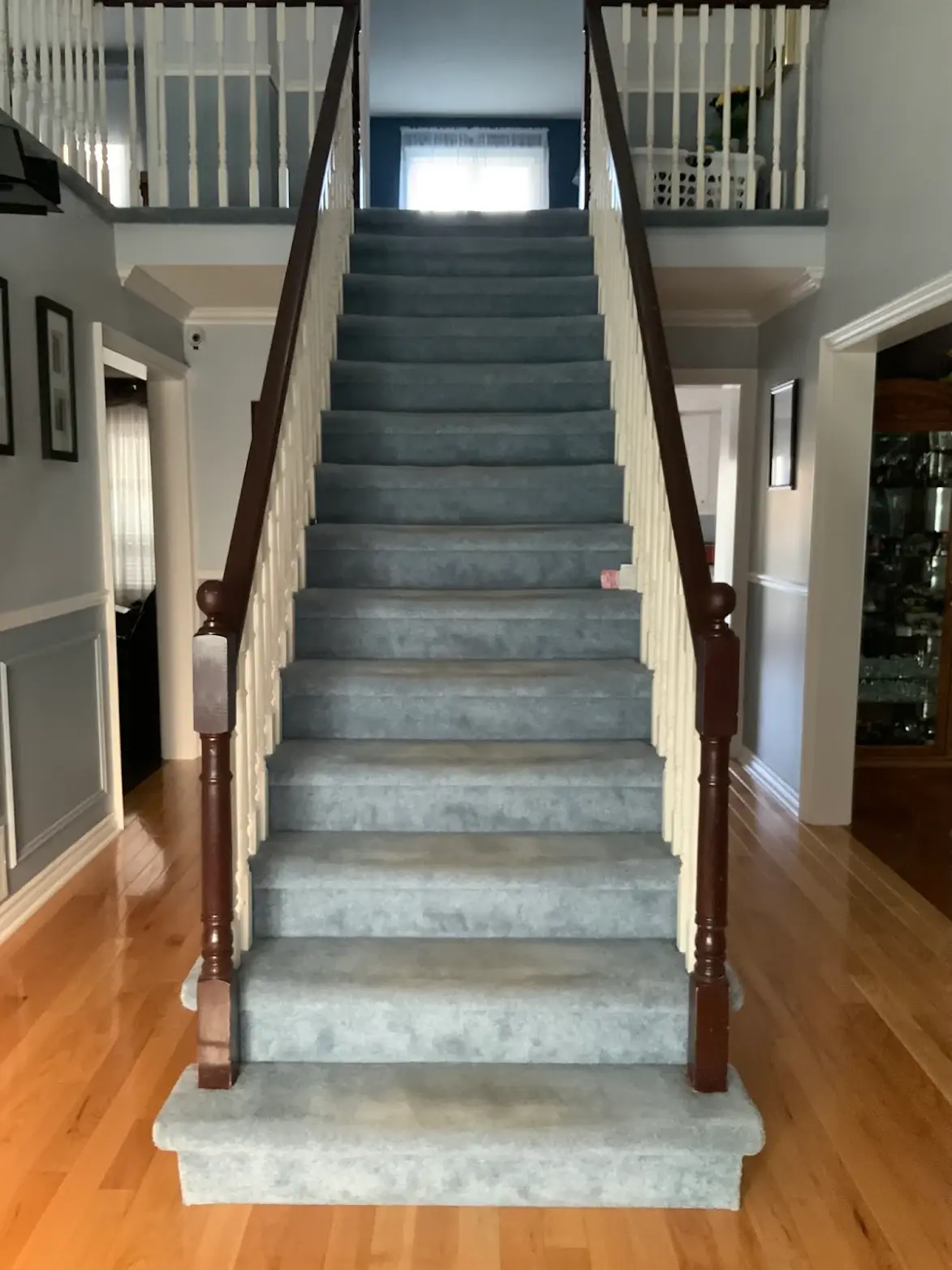 Staircase before renovation with grey carpet, white wood spindles and dark wood handrails.
