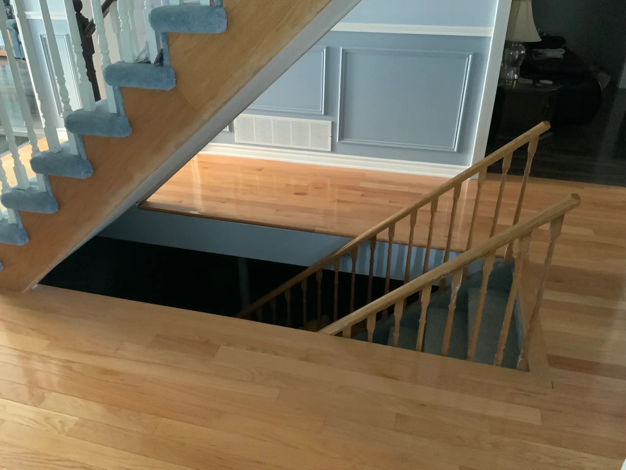 Upper stair landing before renovation with grey carpet and natural wood railings.