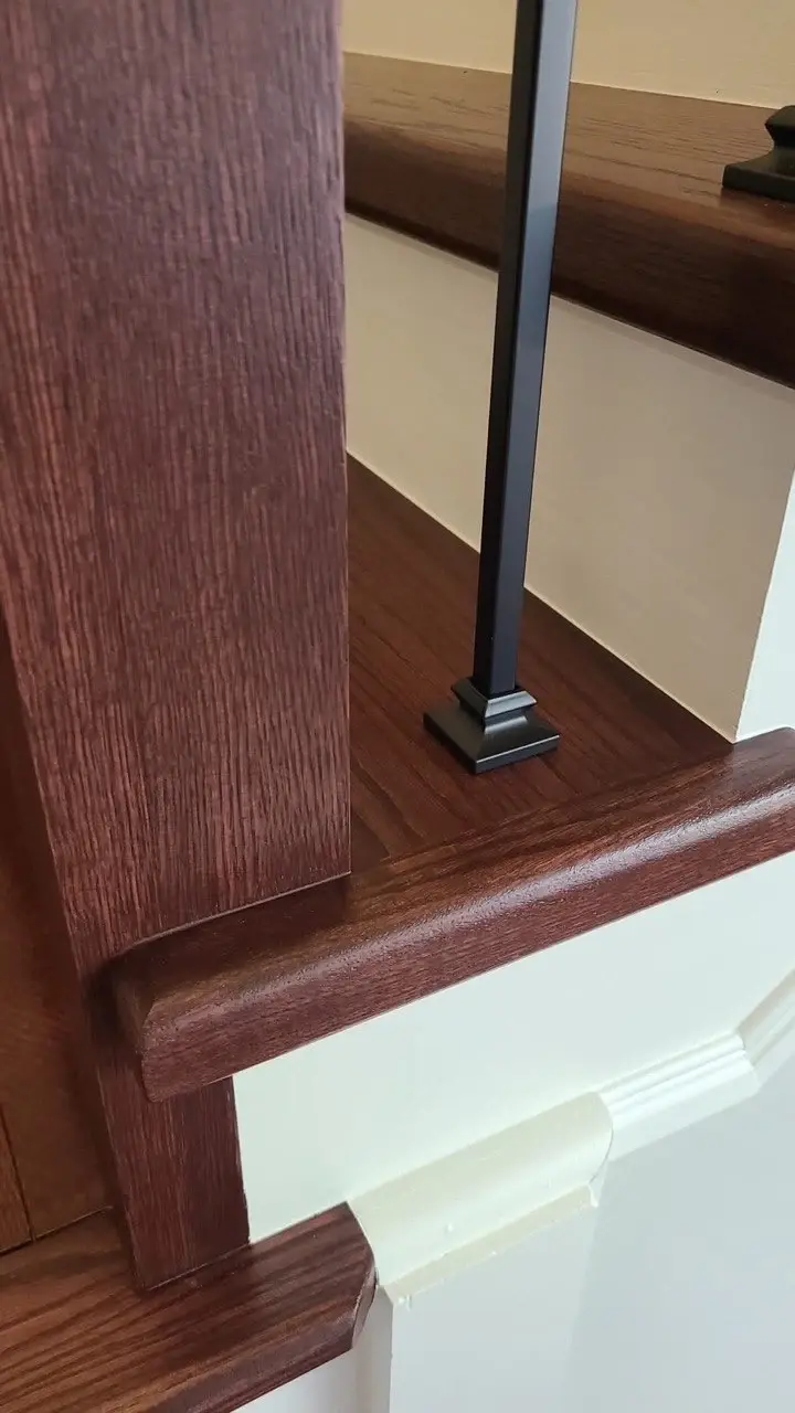 Detail of a stained wood stair tread, newel post and black metal baluster base.