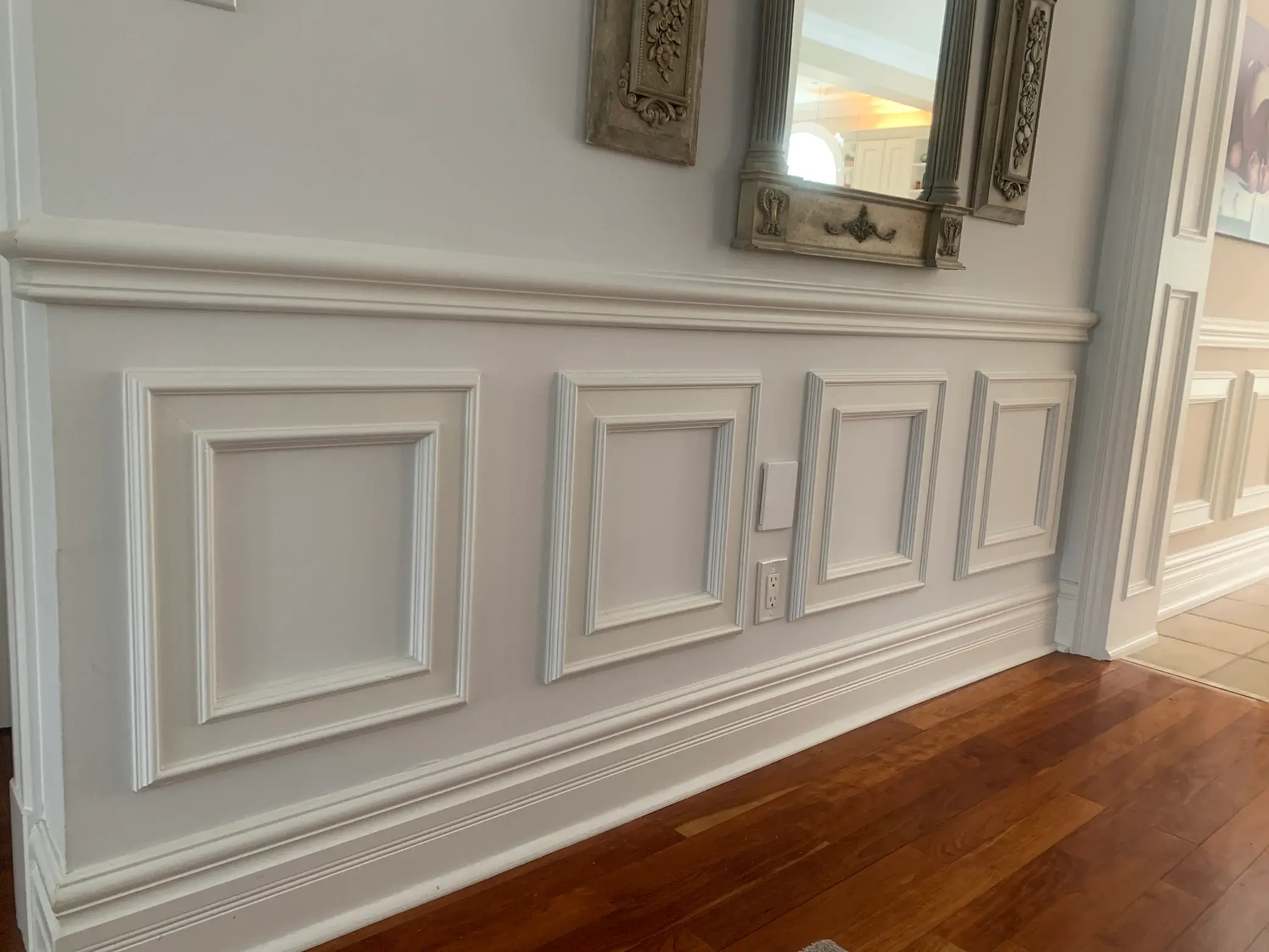 Finished white wainscoting with picture-frame moulding beneath an ornate mirror.