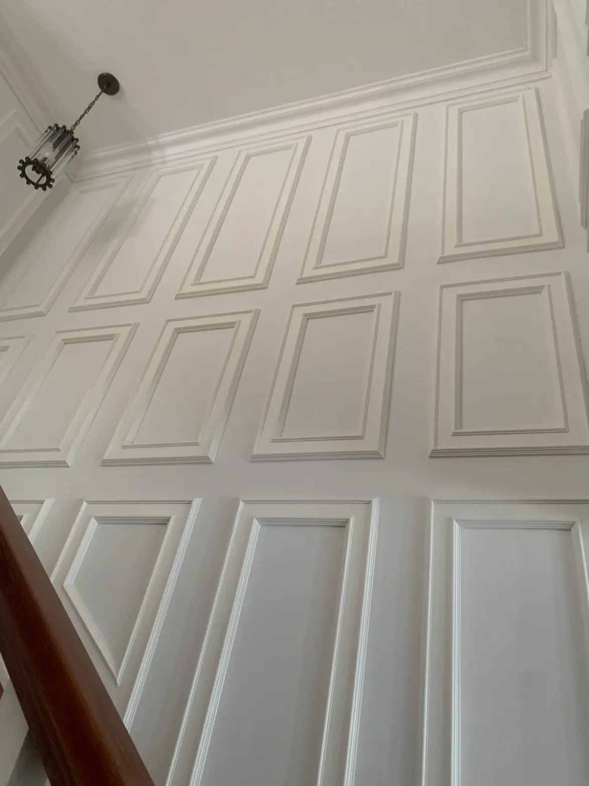 Full-height white picture-frame moulding in a stairwell with crown trim and pendant light.